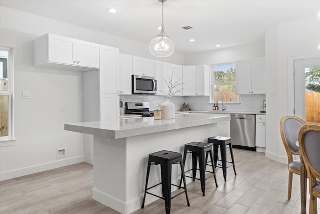 kitchen with a healthy amount of sunlight, a kitchen island, light wood-type flooring, and stainless steel appliances