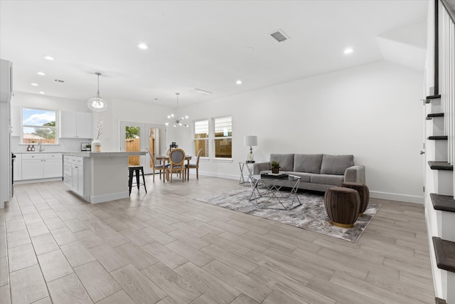 living room with a chandelier, light wood-type flooring, and lofted ceiling