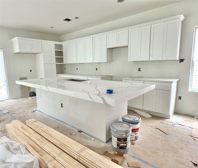 kitchen featuring light stone counters, a center island, and white cabinets