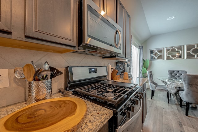 kitchen with lofted ceiling, appliances with stainless steel finishes, light wood-type flooring, and tasteful backsplash