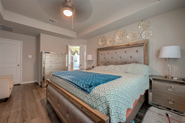 bedroom with wood-type flooring, a raised ceiling, and ceiling fan