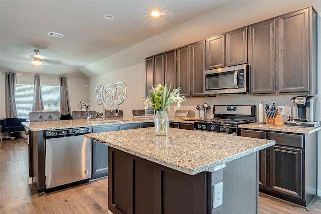 kitchen featuring light stone countertops, light hardwood / wood-style flooring, a center island, stainless steel appliances, and ceiling fan