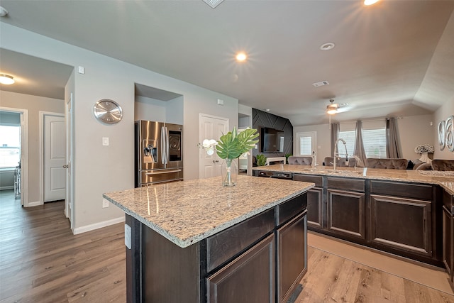 kitchen with dark brown cabinets, light hardwood / wood-style flooring, light stone counters, a center island, and stainless steel refrigerator with ice dispenser