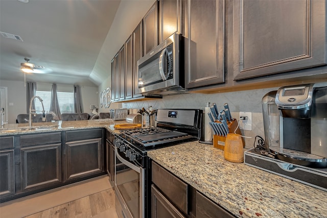 kitchen featuring light hardwood / wood-style flooring, vaulted ceiling, light stone countertops, and appliances with stainless steel finishes