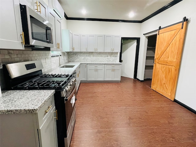 kitchen with light stone countertops, sink, stainless steel appliances, a barn door, and light hardwood / wood-style floors