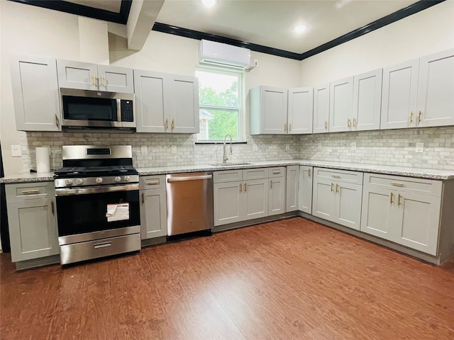 kitchen with decorative backsplash, appliances with stainless steel finishes, light wood-type flooring, a wall unit AC, and sink