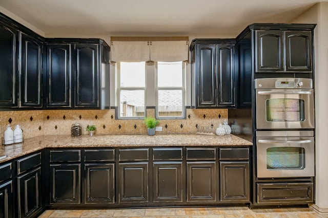 kitchen featuring dark cabinets, stainless steel double oven, and backsplash