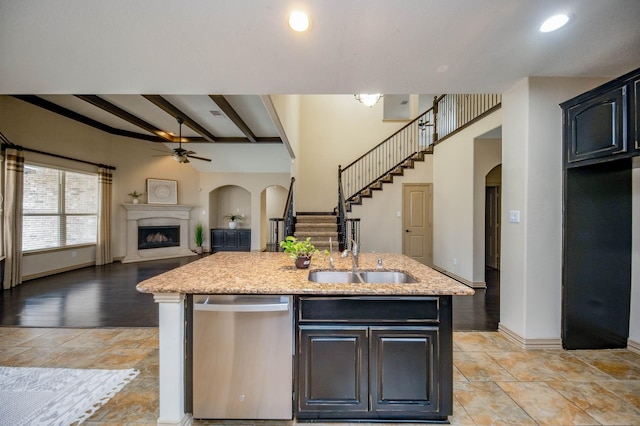 kitchen with arched walkways, a fireplace with raised hearth, dishwasher, open floor plan, and a sink