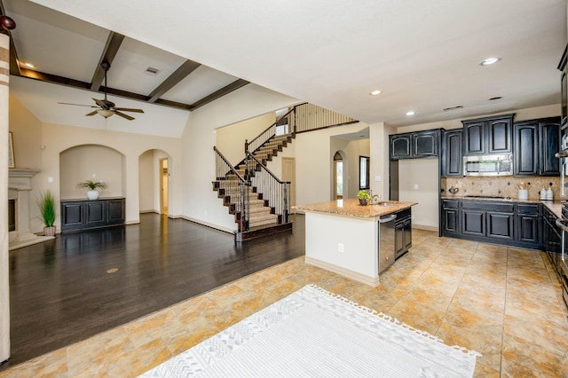 kitchen featuring arched walkways, light stone counters, open floor plan, appliances with stainless steel finishes, and tasteful backsplash