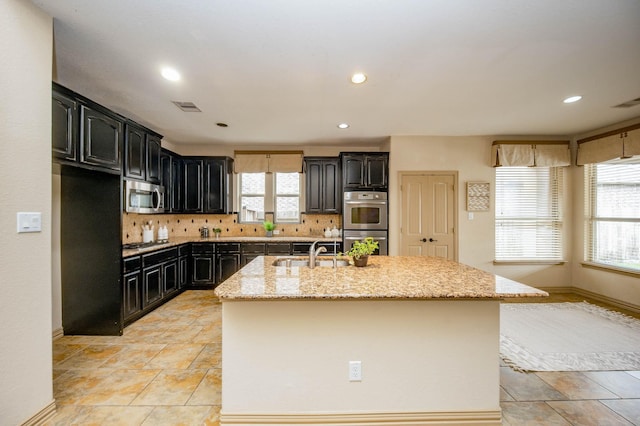 kitchen featuring light stone counters, stainless steel appliances, visible vents, decorative backsplash, and a sink