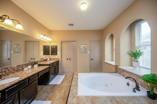 full bathroom featuring a whirlpool tub, double vanity, visible vents, and a sink