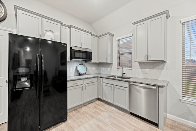 kitchen with lofted ceiling, light stone counters, appliances with stainless steel finishes, light hardwood / wood-style flooring, and sink