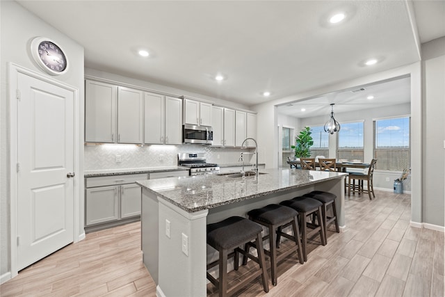 kitchen with an island with sink, gray cabinetry, stainless steel appliances, sink, and light hardwood / wood-style floors