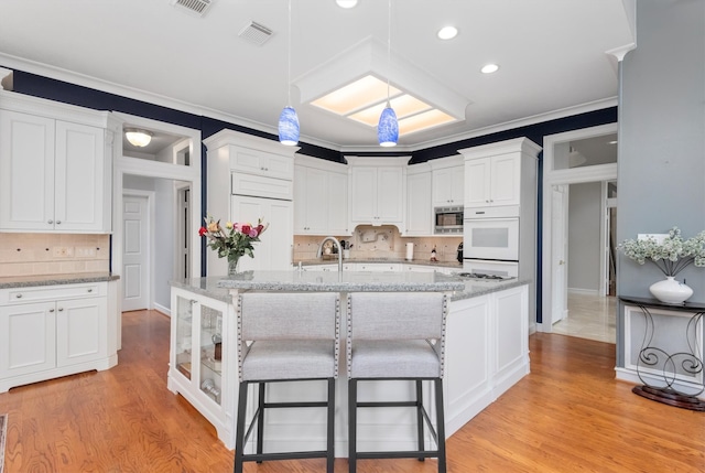 kitchen featuring light wood-type flooring, crown molding, backsplash, stainless steel microwave, and white cabinets