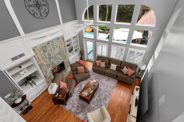 living room featuring ceiling fan, a stone fireplace, wood-type flooring, and a high ceiling