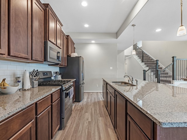 kitchen with stainless steel appliances, sink, decorative backsplash, light stone countertops, and light hardwood / wood-style floors