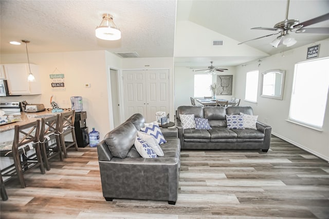 living room with lofted ceiling, hardwood / wood-style floors, ceiling fan, and a textured ceiling