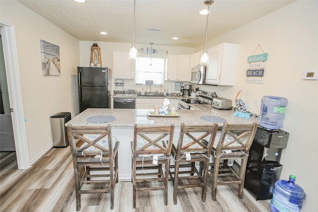 kitchen featuring a breakfast bar, kitchen peninsula, appliances with stainless steel finishes, light hardwood / wood-style flooring, and white cabinets