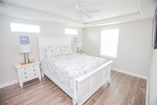 bedroom with ceiling fan, multiple windows, a tray ceiling, and wood-type flooring