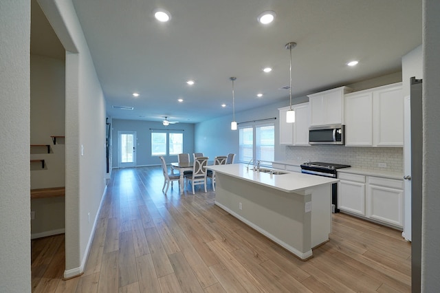 kitchen with decorative light fixtures, a kitchen island with sink, white cabinetry, appliances with stainless steel finishes, and light wood-type flooring