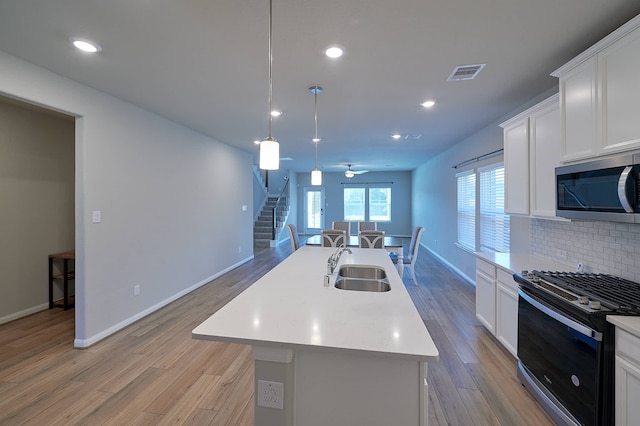 kitchen with white cabinets, pendant lighting, light wood-type flooring, black gas range, and a center island with sink