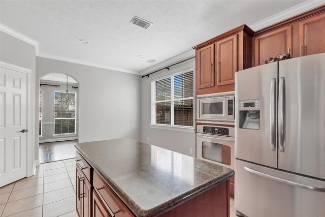 kitchen featuring dark stone countertops, ornamental molding, stainless steel appliances, a kitchen island, and light tile patterned flooring