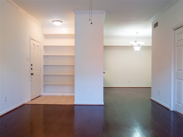 spare room featuring built in features, hardwood / wood-style flooring, an inviting chandelier, and ornamental molding