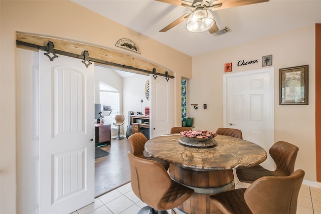 dining room with light hardwood / wood-style flooring, ceiling fan, and a barn door