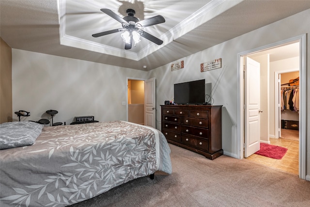 carpeted bedroom with a closet, a spacious closet, a raised ceiling, ceiling fan, and ornamental molding