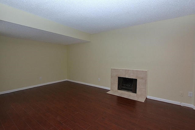 unfurnished living room featuring a tiled fireplace, dark hardwood / wood-style floors, and a textured ceiling