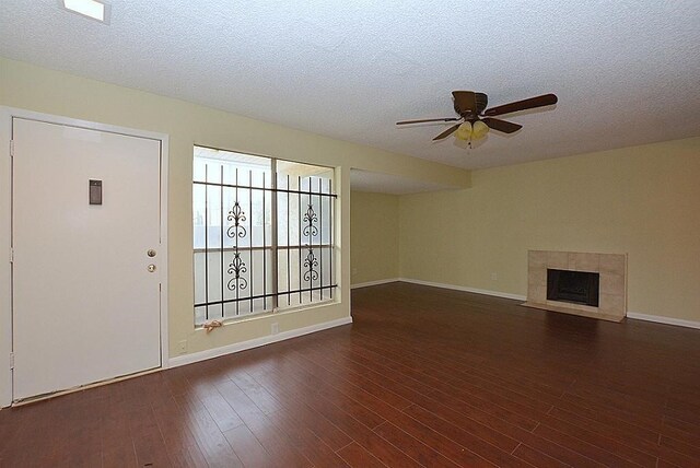 unfurnished living room featuring dark wood-type flooring, a textured ceiling, ceiling fan, and a tile fireplace