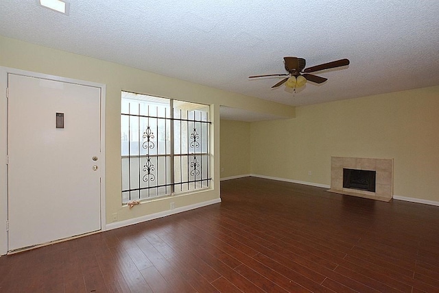 unfurnished living room featuring a ceiling fan, dark wood-style floors, baseboards, a fireplace, and a textured ceiling