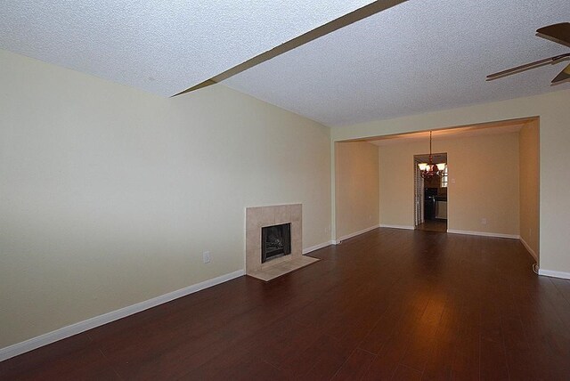 unfurnished living room featuring ceiling fan with notable chandelier, a tile fireplace, dark hardwood / wood-style flooring, and a textured ceiling