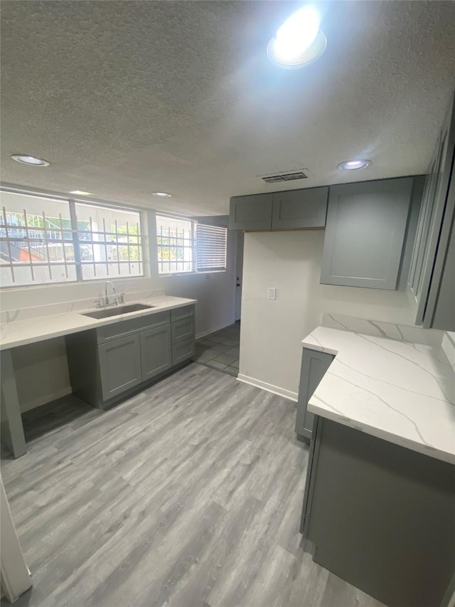 kitchen featuring gray cabinets, a sink, a textured ceiling, light wood finished floors, and light stone countertops