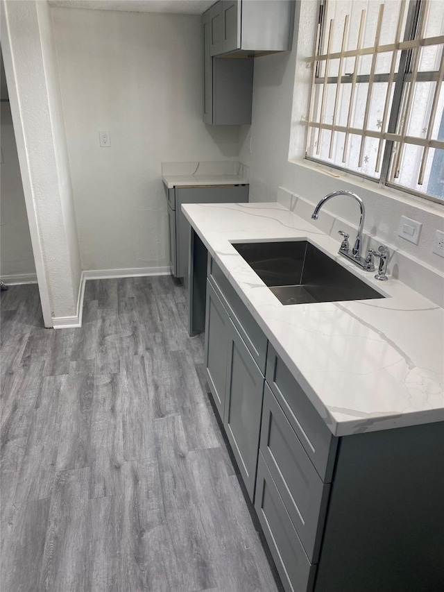 kitchen featuring light stone countertops, gray cabinets, a wealth of natural light, and a sink