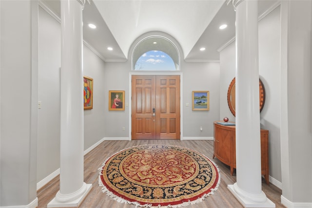 entryway featuring light wood-type flooring, crown molding, lofted ceiling, and ornate columns