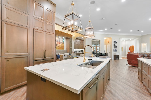 kitchen featuring light stone counters, a center island with sink, sink, and light hardwood / wood-style floors