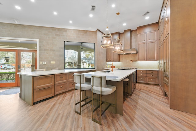 kitchen featuring a kitchen island with sink, wall chimney exhaust hood, and light wood-type flooring