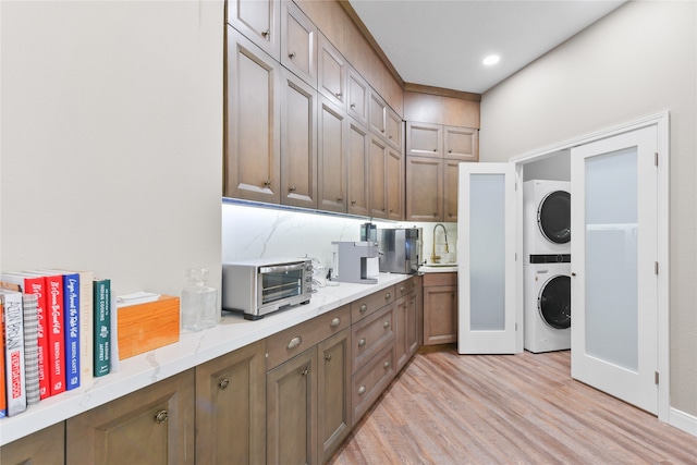 kitchen with light wood-type flooring, sink, tasteful backsplash, and stacked washer / drying machine