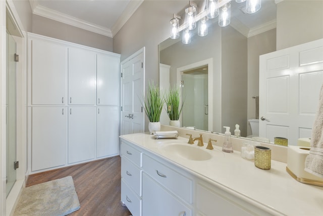 bathroom featuring hardwood / wood-style flooring, a shower with door, toilet, vanity, and ornamental molding