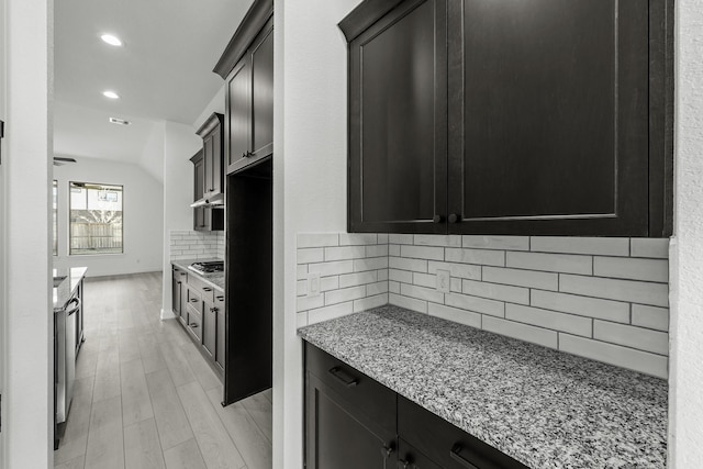 kitchen featuring stainless steel gas stovetop, backsplash, light stone counters, and light hardwood / wood-style floors