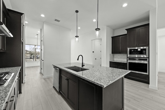 kitchen featuring pendant lighting, sink, a kitchen island with sink, stainless steel appliances, and light stone countertops