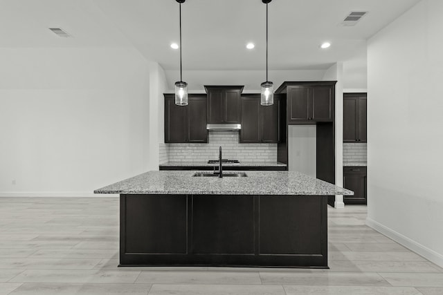 kitchen featuring light stone countertops, an island with sink, and hanging light fixtures