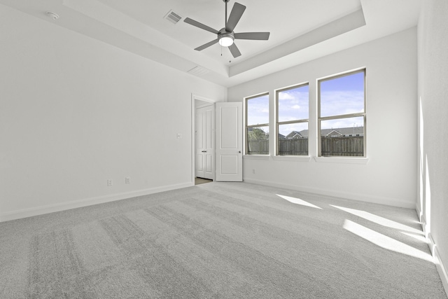 empty room featuring a tray ceiling, light colored carpet, and ceiling fan