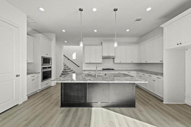 kitchen with white cabinetry, stainless steel appliances, light stone countertops, a center island with sink, and decorative light fixtures