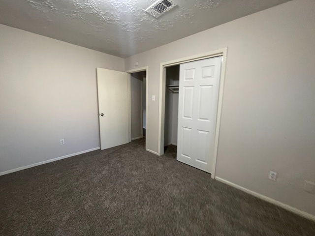 unfurnished bedroom with a textured ceiling, dark colored carpet, and a closet