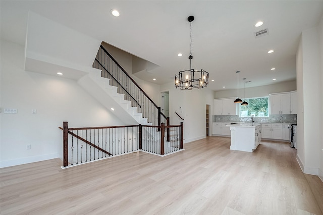 kitchen with pendant lighting, white cabinetry, tasteful backsplash, a kitchen island, and light wood-type flooring