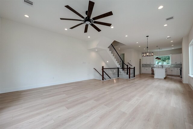 unfurnished living room featuring ceiling fan with notable chandelier and light hardwood / wood-style flooring