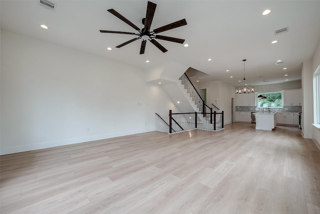 unfurnished living room featuring ceiling fan with notable chandelier and light hardwood / wood-style flooring