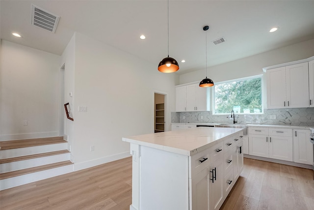 kitchen featuring hanging light fixtures, white cabinetry, light stone countertops, a kitchen island, and decorative backsplash